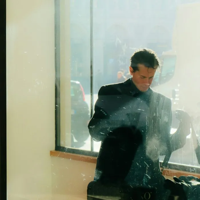 Ein Mann in dunklem Mantel hinter einem sonnenbeschienenen Bürofenster