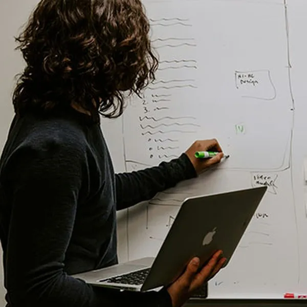 Eine Frau mit einem Laptop in der Hand schreibt Notizen auf ein Whiteboard