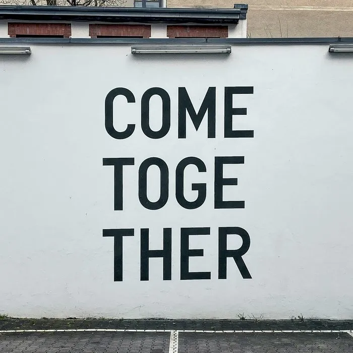 Eine weiße Wand mit den Worten „Come together“ in großen schwarzen Buchstaben